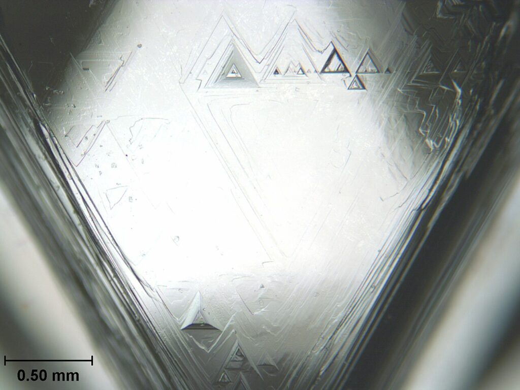 Trygony na ścianie surowego kryształu diamentu naturalnego pod mikroskopem